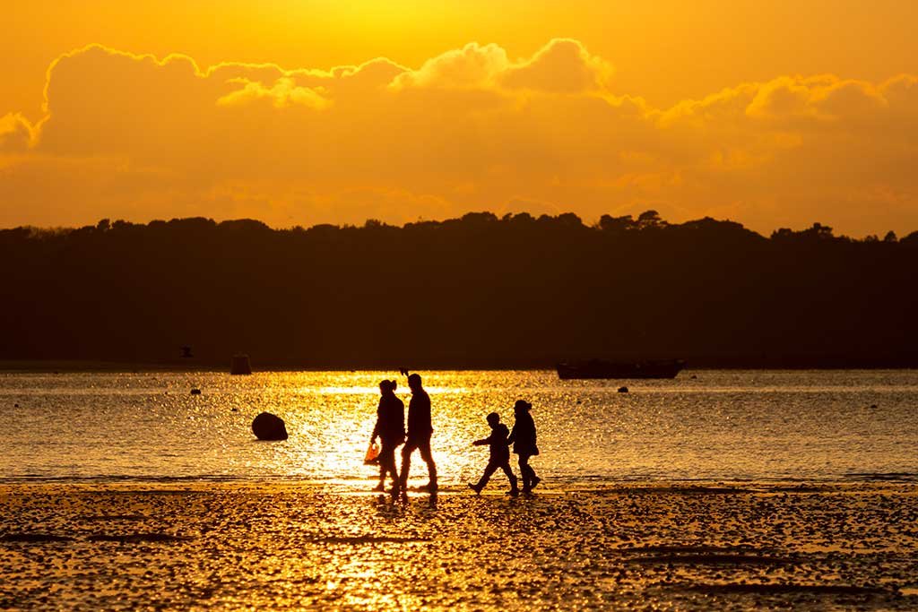 A family walks along the beach at sunset at the bottom of Evening Hill. 